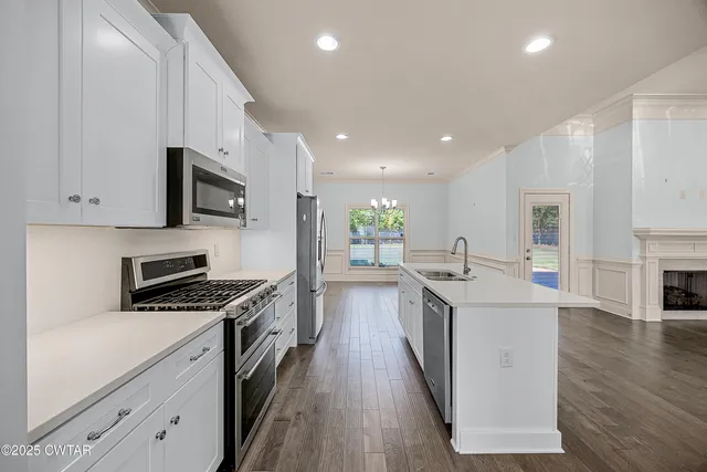 a kitchen with stainless steel appliances a sink dishwasher a stove top oven a refrigerator with white cabinets and wooden floor