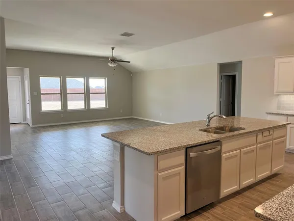 a kitchen with kitchen island granite countertop a sink a stove top oven and white cabinets