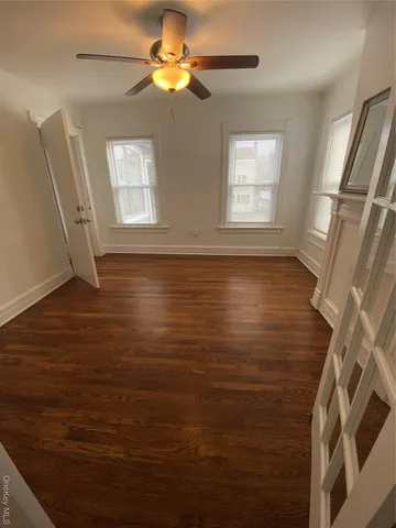 a view of an empty room with window and hardwood floor