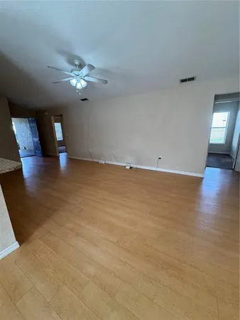 a view of an empty room with chandelier fan and wooden floor
