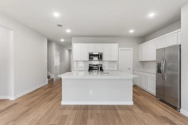 a large kitchen with stainless steel appliances a large counter top a stove and a refrigerator