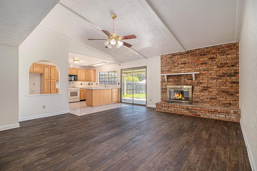 1814 Addington Drive Carrollton, TX 75007 - Photo 7 of 24 Unfurnished living room with hardwood / wood-style flooring, a fireplace, ceiling fan, a textured ceiling, and vaulted ceiling