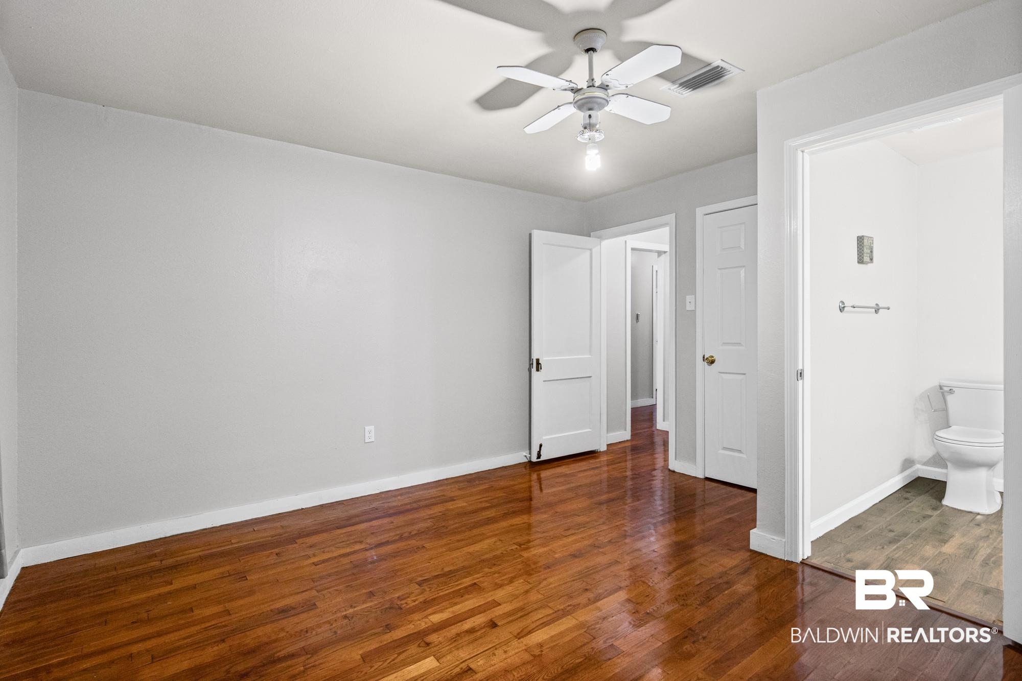 312 Sutherland Drive Mobile, AL 36611 - Photo 15 of 28 Primary bedroom featuring rich wood-finish flooring, light gray wall paint, a ceiling fan with integrated lighting, and multiple interior doorways
