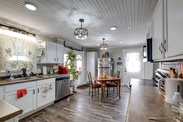 a kitchen with stainless steel appliances granite countertop a stove a sink dishwasher and white cabinets with wooden floor