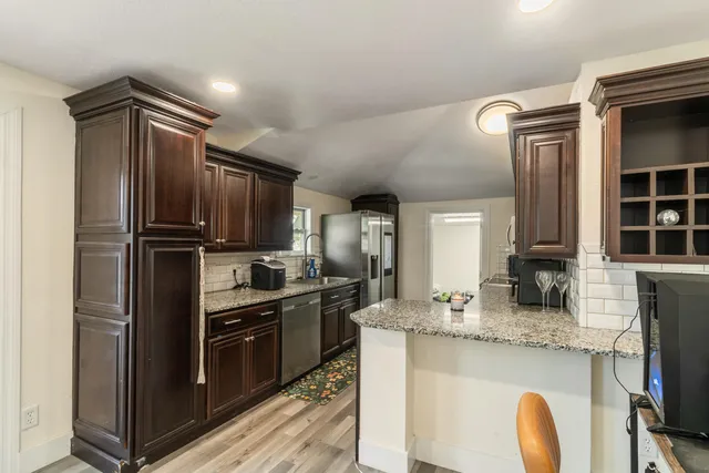 a kitchen with granite countertop stainless steel appliances a sink stove refrigerator and cabinets
