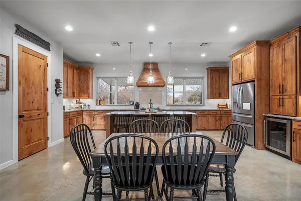 a kitchen with stainless steel appliances granite countertop a dining table chairs refrigerator and sink