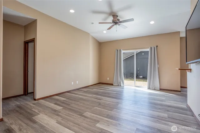 a view of an empty room with wooden floor and a ceiling fan