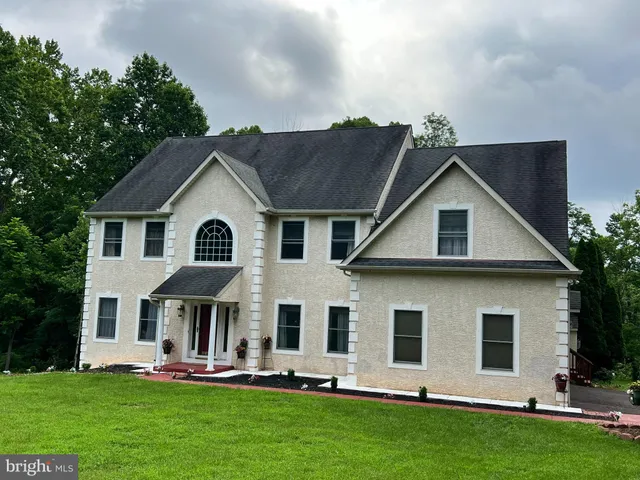 a view of a white house with large windows and a yard with plants and large trees