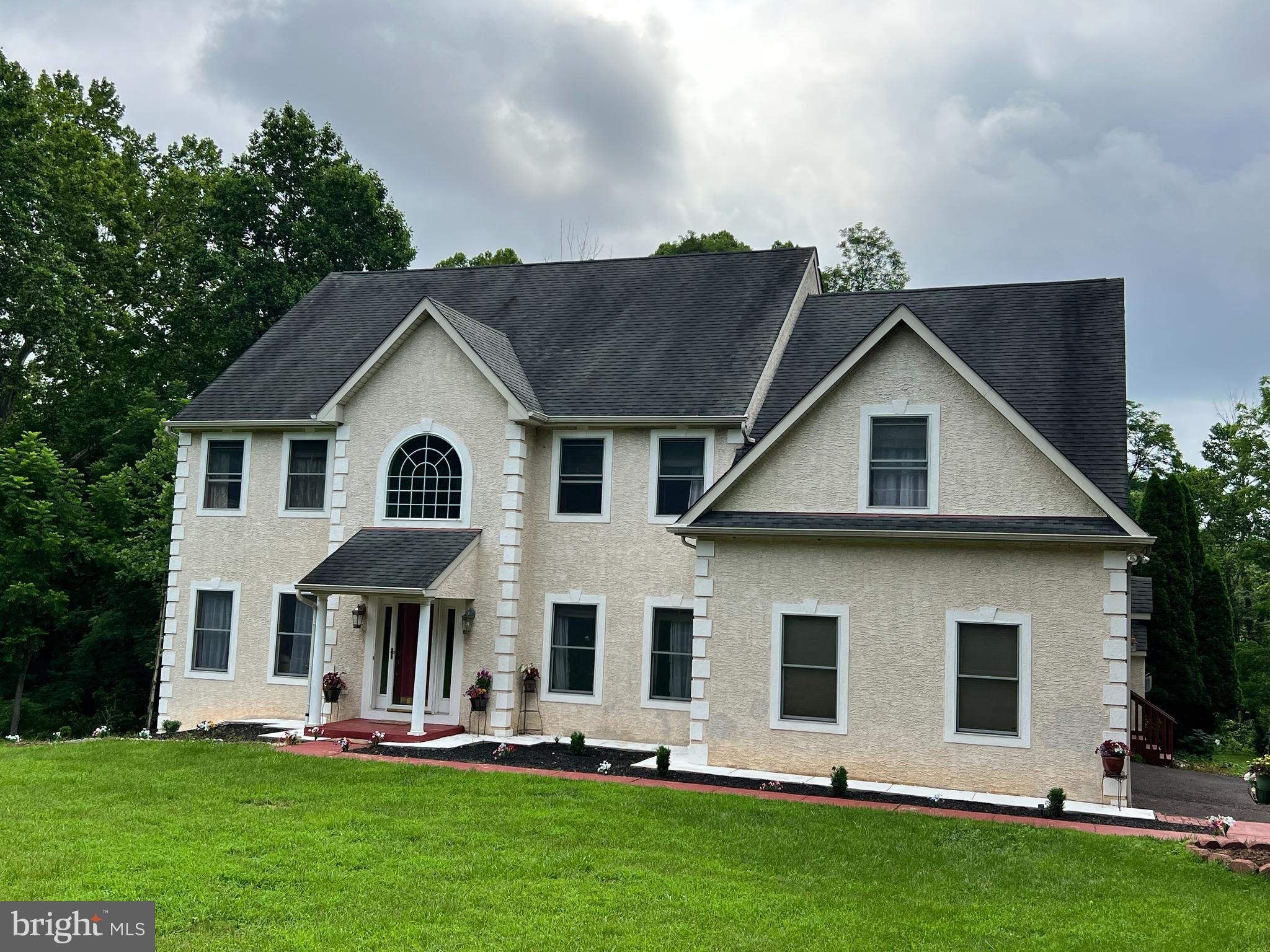 a view of a white house with large windows and a yard with plants and large trees