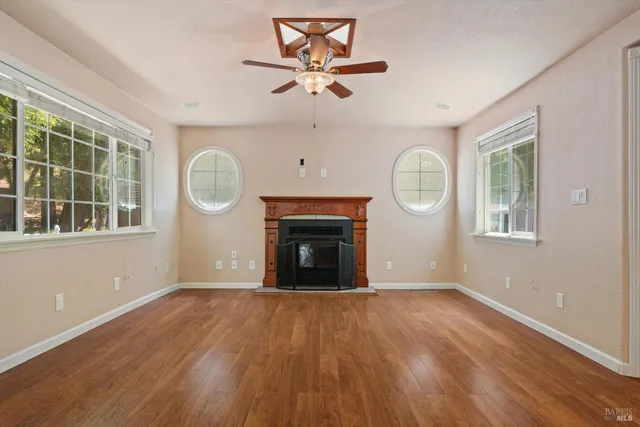 an empty room with windows a fireplace a ceiling fan and wooden floor