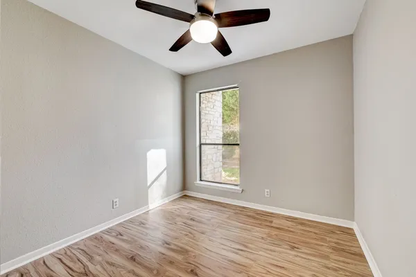an empty room with wooden floor chandelier fan and windows