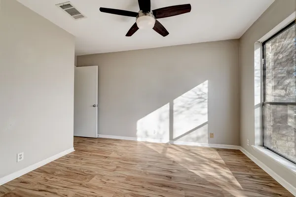 an empty room with wooden floor fan and windows