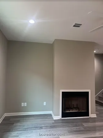 a view of an empty room with wooden floor and fireplace
