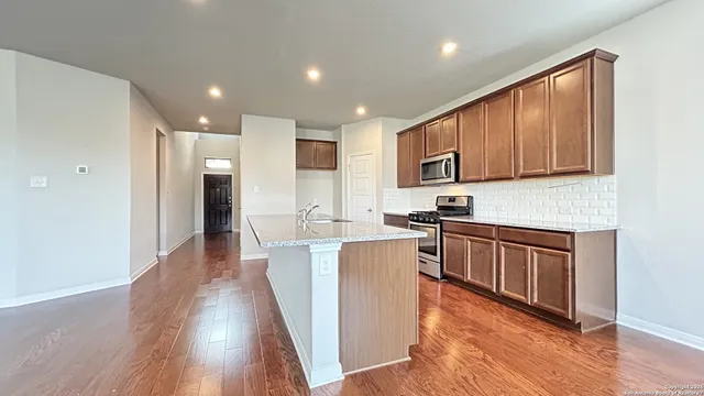 a kitchen with stainless steel appliances granite countertop wooden cabinets a refrigerator a sink a stove a microwave and wooden floors