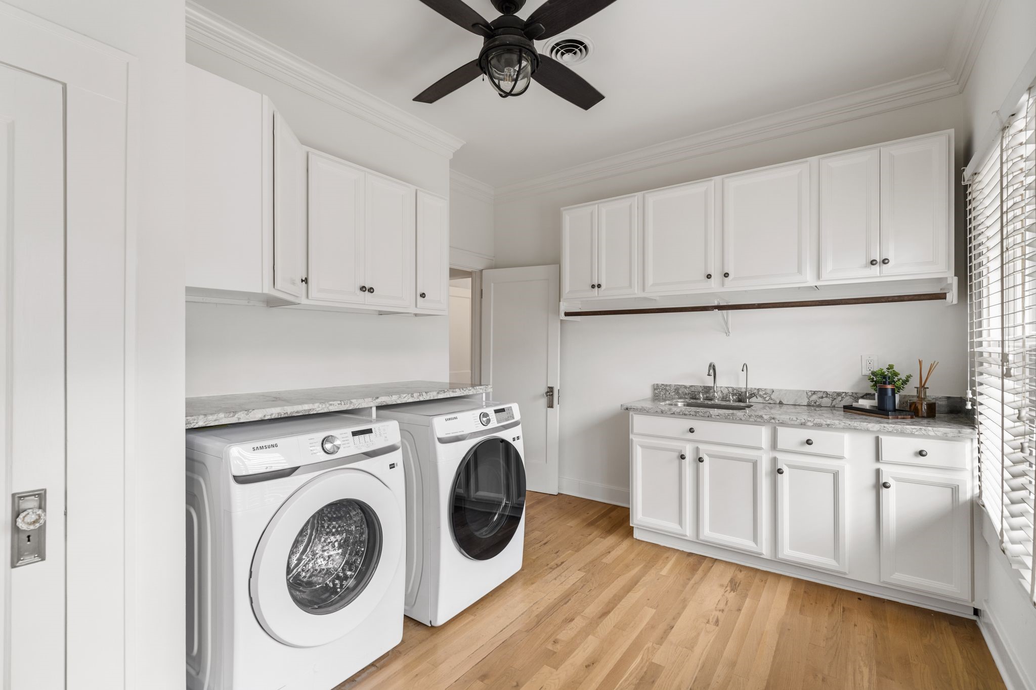 307 East 8th Street Houston, TX 77007 - Photo 23 of 35 Exceptionally spacious utility and mudroom designed with everyday convenience in mind. Features include a new washer and dryer (2026), extensive countertop space for folding, a utility sink, hanging rod for clothing, and abundant cabinetry plus an additional storage closet for excellent organization. Hardwood flooring, a ceiling fan, and direct access to the side deck and driveway make loading and unloading groceries, laundry, and everyday essentials effortless.