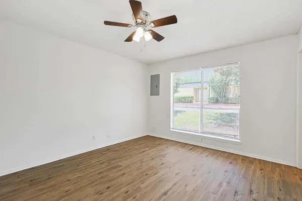 an empty room with wooden floor fan and windows