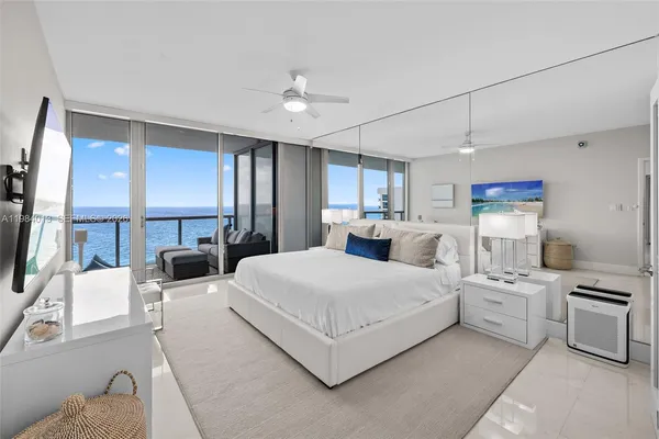 a large white bedroom with a large bed a flat tv screen and furniture