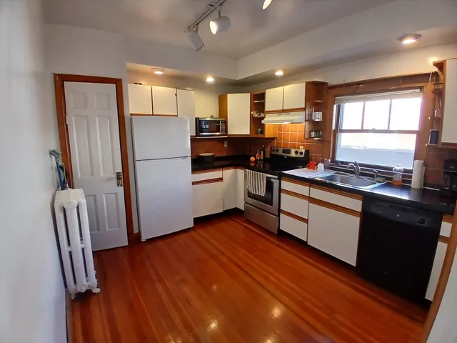 a kitchen with stainless steel appliances granite countertop a refrigerator a sink dishwasher a stove and white countertops with wooden floor