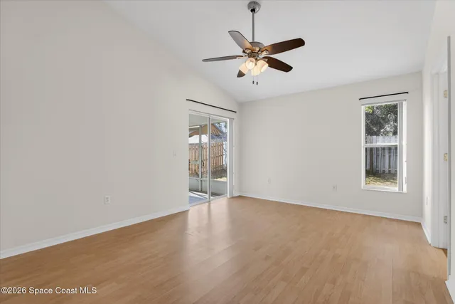 an empty room with wooden floor fan and windows