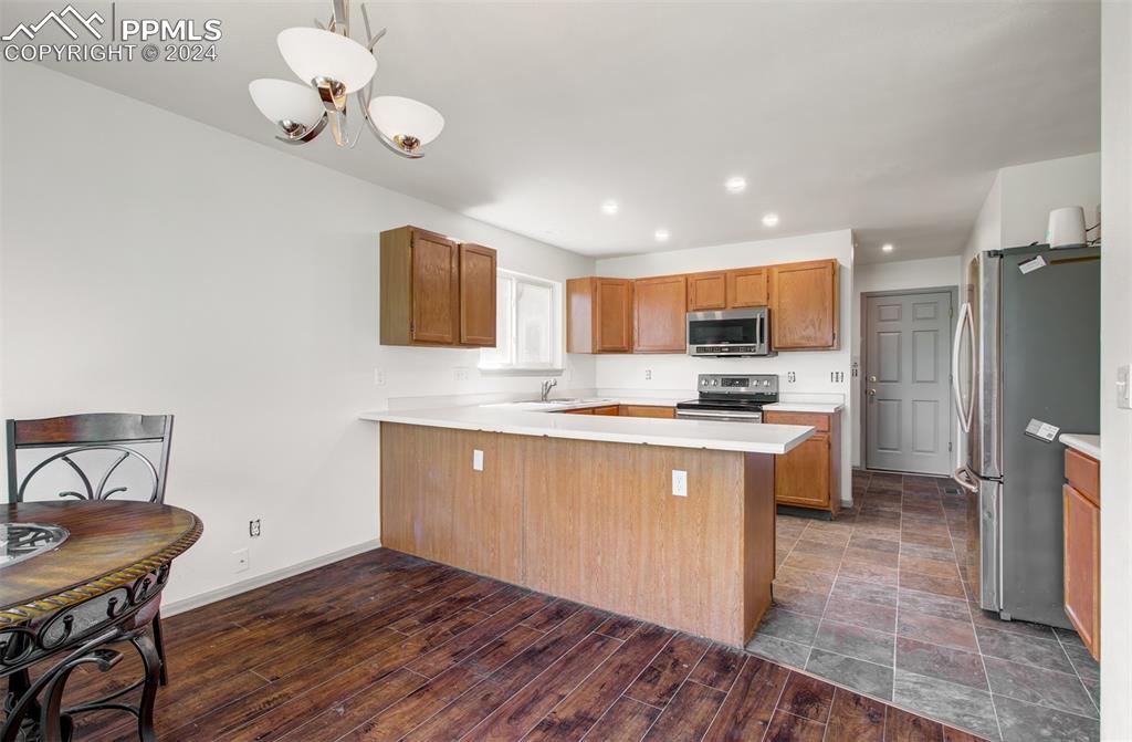 4176 South Himalaya Way Aurora, CO 80013 - Photo 10 of 27 Kitchen featuring an inviting chandelier, kitchen peninsula, dark wood-type flooring, hanging light fixtures, and appliances with stainless steel finishes