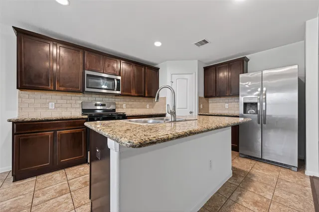 a kitchen with stainless steel appliances granite countertop a refrigerator a stove a sink and a microwave