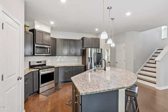 a kitchen with kitchen island granite countertop a table chairs refrigerator and microwave