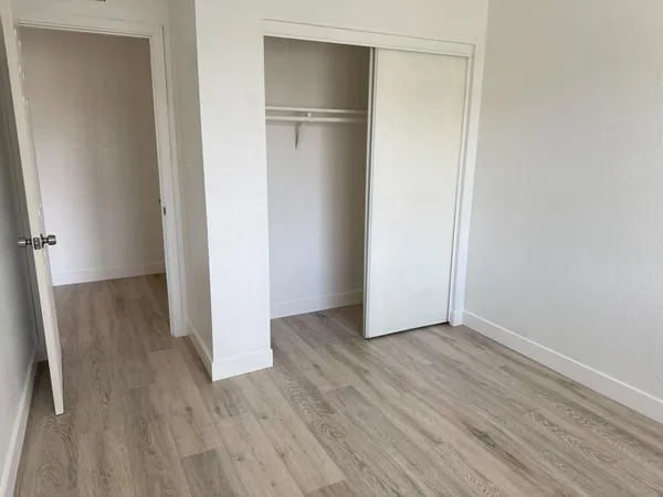 a view of an empty room with wooden floor and closet