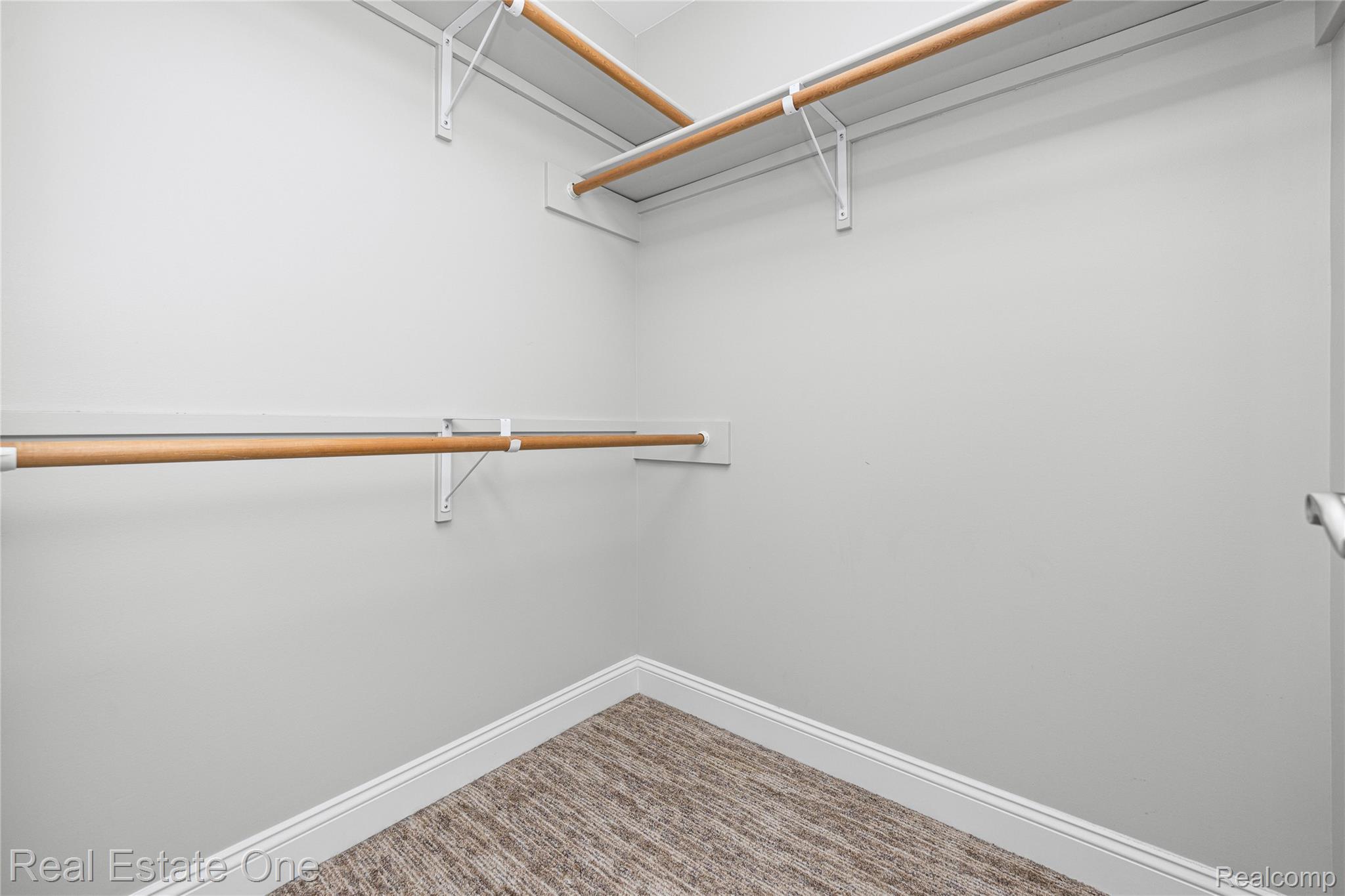 2479 Gibson Road Grand Blanc, MI 48439 - Photo 35 of 55 Spacious walk-in closet featuring light grey walls, white baseboards, a textured carpet, and multiple wood-finish hanging rods with white shelving