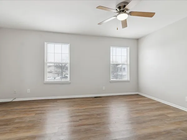 an empty room with wooden floor chandelier fan and windows