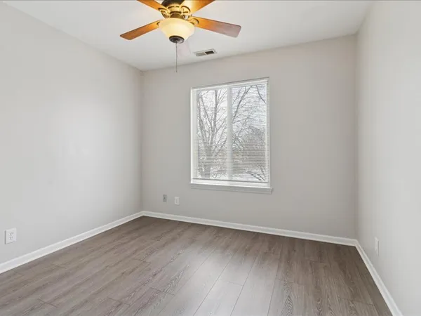 an empty room with wooden floor chandelier fan and windows