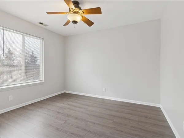 an empty room with wooden floor fan and windows
