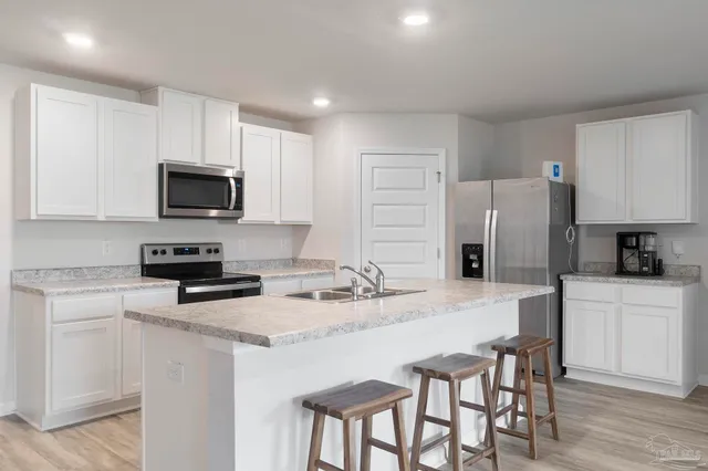 a kitchen with stainless steel appliances granite countertop a stove a sink a microwave a refrigerator and white cabinets with wooden floor