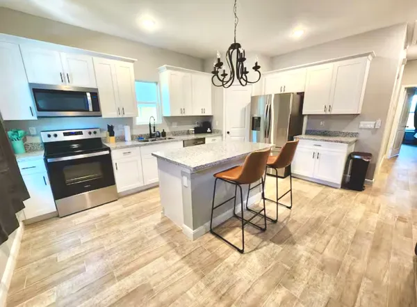 a kitchen with stainless steel appliances kitchen island granite countertop a refrigerator a stove top oven a sink dishwasher and white cabinets with wooden floor