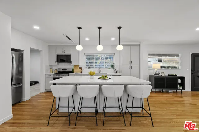 a kitchen with stainless steel appliances kitchen island granite countertop a dining table chairs and a refrigerator