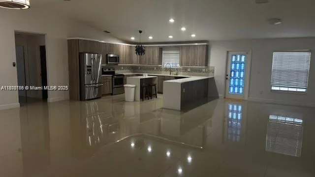 a open kitchen with stainless steel appliances kitchen island granite countertop a refrigerator a stove a sink and a dining table with wooden floor