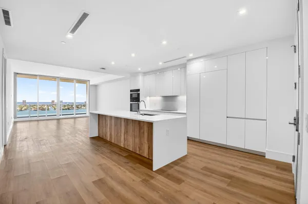 a view of a kitchen with kitchen island a sink wooden floor and stainless steel appliances