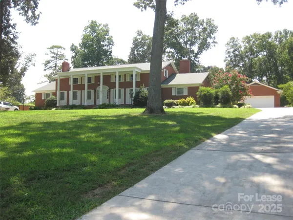 a view of a house next to a big yard and large trees