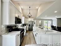 275 Sound Road Greenport, NY 11944 - Photo 15 of 28 Kitchen featuring white cabinets, appliances with stainless steel finishes, lofted ceiling, a large island, and decorative light fixtures