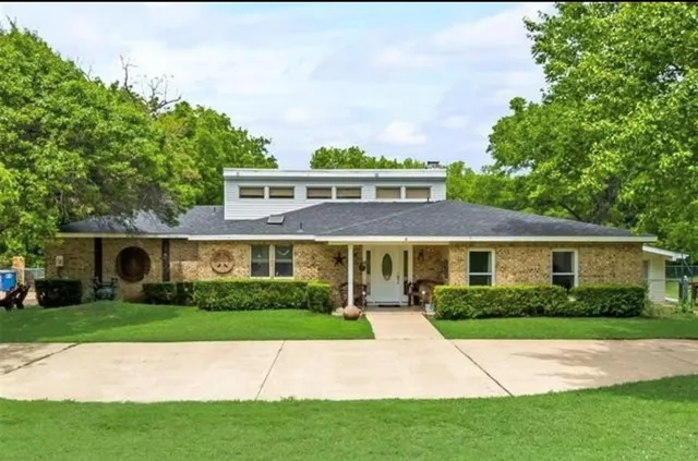 a view of house in front of a big yard with large trees