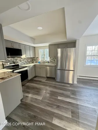 a kitchen with stainless steel appliances granite countertop a stove top oven a sink a refrigerator white cabinets and wooden floor