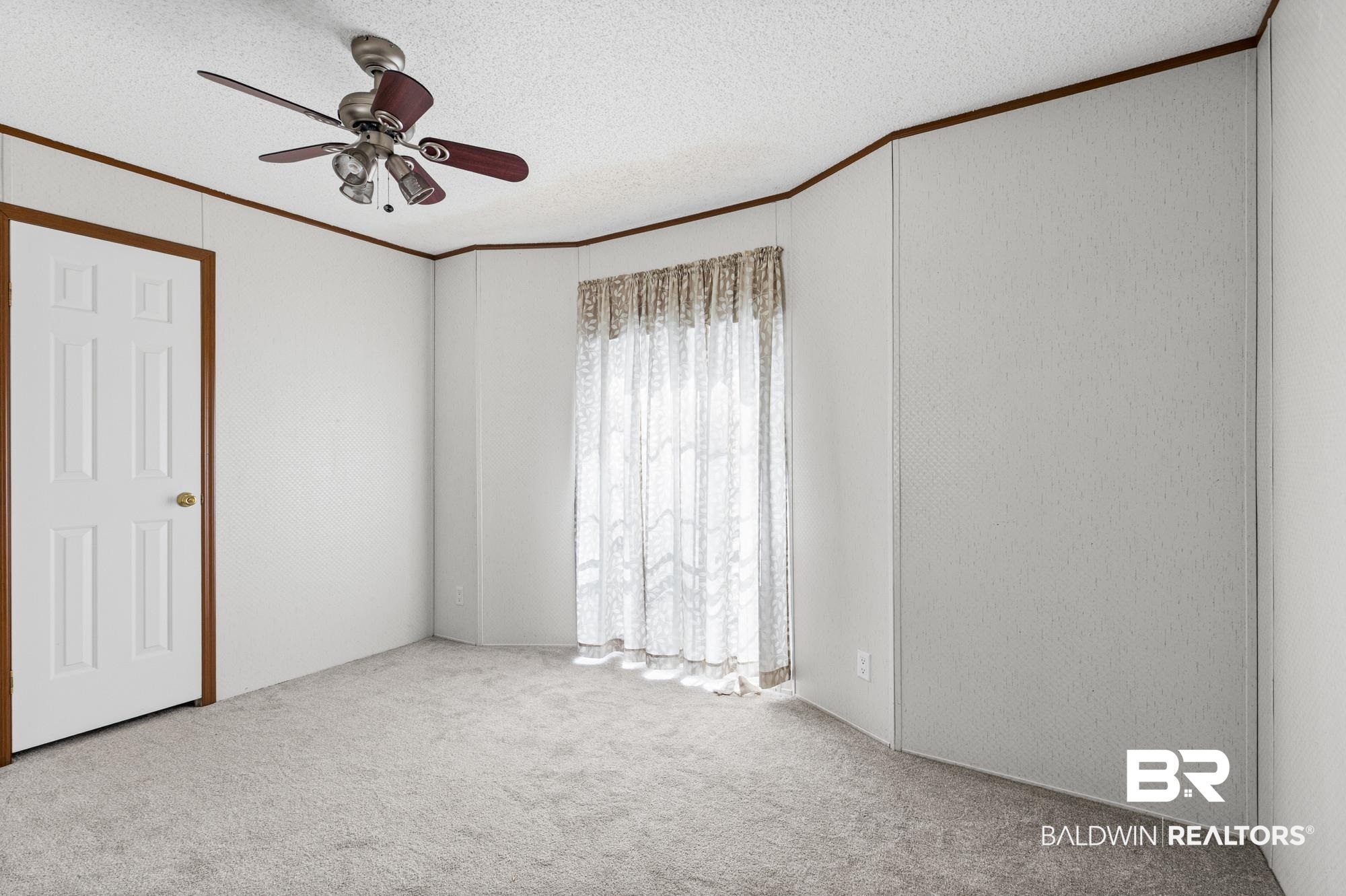 8675 Hunters Pointe Drive North Theodore, AL 36582 - Photo 14 of 20 Carpeted room featuring a white paneled door with wood-finish trim, a ceiling fan with light fixture, and window with sheer curtains