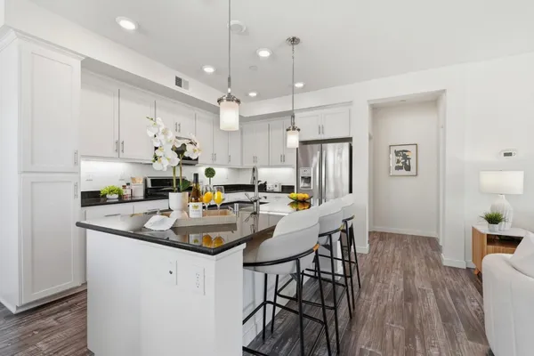 a kitchen with stainless steel appliances granite countertop a refrigerator a sink a stove and white cabinets with wooden floor