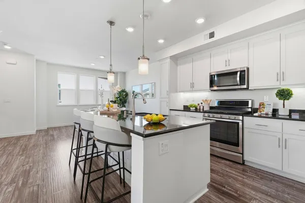 a kitchen with stainless steel appliances kitchen island granite countertop a stove top oven a sink a dining table and chairs with wooden floor