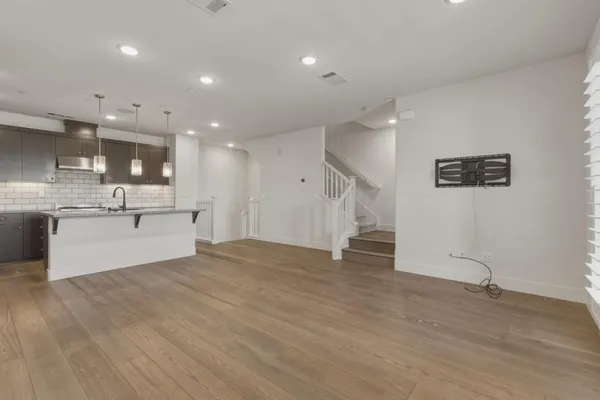 a view of an empty room with wooden floor and a kitchen