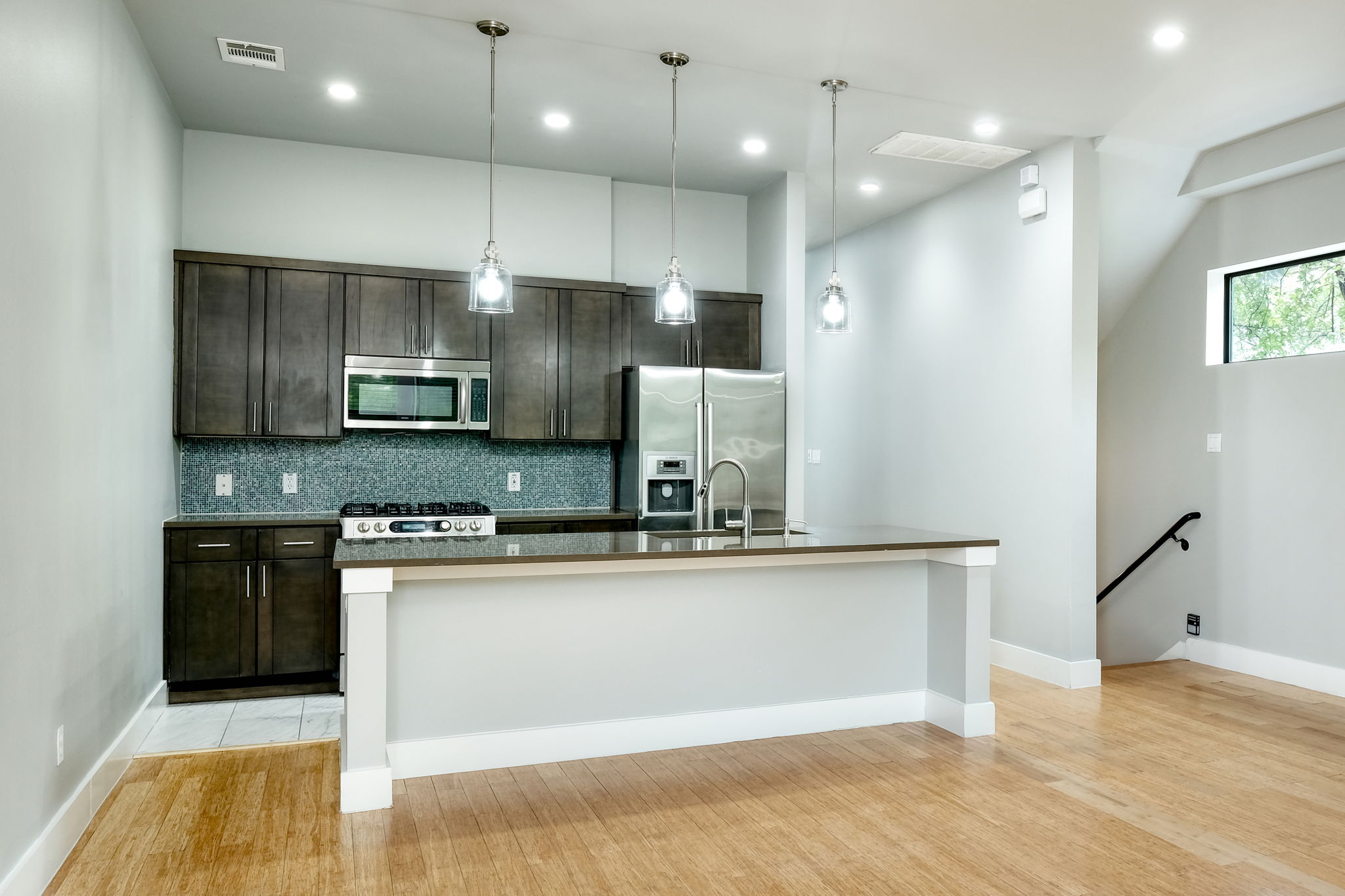 3000 Speedway Street, Unit E Austin, TX 78705 - Photo 2 of 16 A contemporary kitchen showcasing dark wood cabinetry, stainless steel appliances, and a central island with pendant lighting.