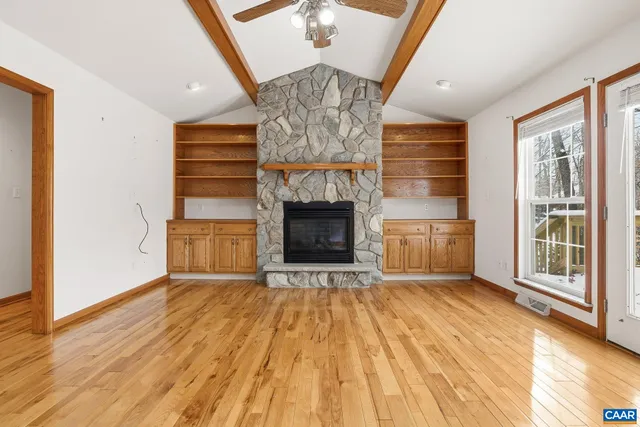 a view of an empty room with wooden floor fireplace and a window