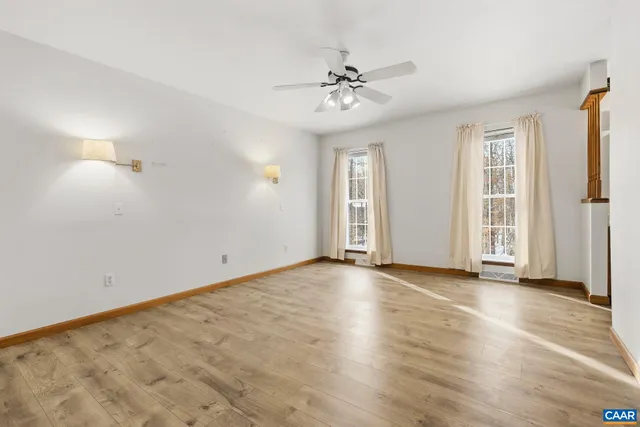an empty room with wooden floor chandelier fan and windows