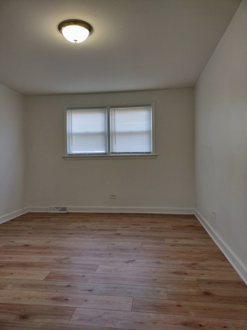 7910 South Muskegon Avenue, Unit 3 Chicago, IL 60617 - Photo 9 of 17 a view of an empty room with wooden floor and a window