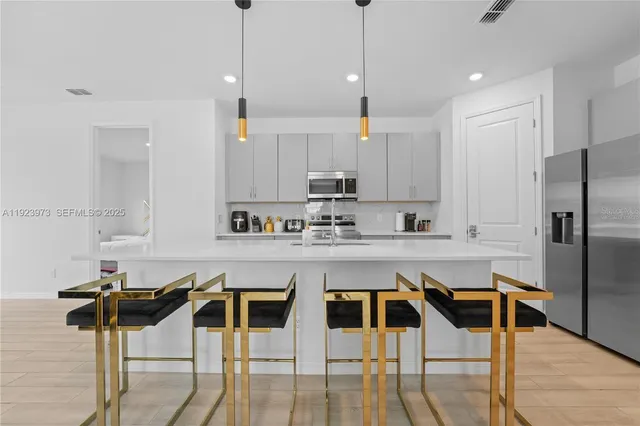 a kitchen with stainless steel appliances kitchen island granite countertop a dining table chairs and white cabinets