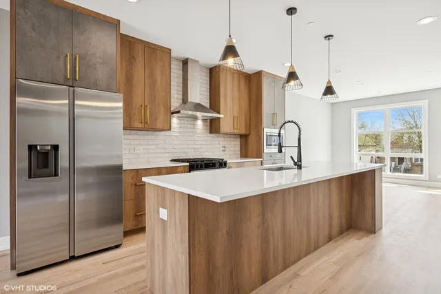 a kitchen with stainless steel appliances a sink a refrigerator a center island a stove and a wooden floors